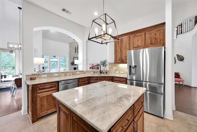5451 Harvest Oak Landing Dr, Spring, TX 77386 - kitchen with stainless steel appliances, a chandelier, light stone countertops, arched walkways, and brown cabinetry