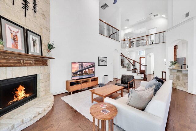 5451 Harvest Oak Landing Dr, Spring, TX 77386 - living area featuring arched walkways, a stone fireplace, a towering ceiling, wood-type flooring, and stairs