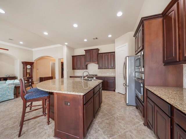 5411 Cedar Elm Ln, Fulshear, TX 77441 - kitchen featuring arched walkways, appliances with stainless steel finishes, decorative backsplash, open floor plan, and light stone counters