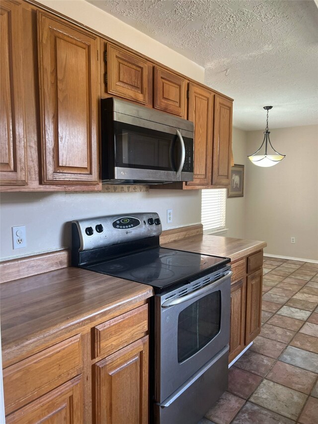 2134 Collingsfield Dr, Sugar Land, TX 77478 - kitchen featuring appliances with stainless steel finishes, brown cabinetry, decorative light fixtures, stone finish floors, and a textured ceiling