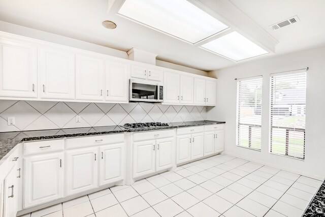 3920 Blackberry Ln, Port Arthur, TX 77642 - kitchen featuring stainless steel microwave, decorative backsplash, dark stone counters, gas stovetop, and white cabinets