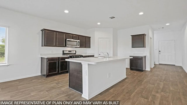 23780 Patchouli Terrace Dr, Splendora, TX 77372 - kitchen with appliances with stainless steel finishes, light wood-style floors, light countertops, a kitchen island with sink, and dark brown cabinetry