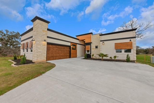 209 Horse Shoe Trl, Angleton, TX 77515 - contemporary home featuring concrete driveway, a garage, a front lawn, stucco siding, and stone siding