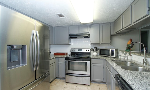 12662 Hackberry Dr, Willis, TX 77318 - kitchen with appliances with stainless steel finishes, gray cabinetry, under cabinet range hood, a sink, and a textured ceiling