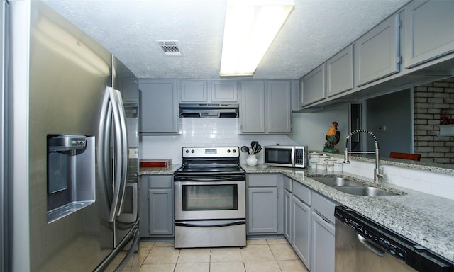 12662 Hackberry Dr, Willis, TX 77318 - kitchen with appliances with stainless steel finishes, under cabinet range hood, a sink, gray cabinets, and decorative backsplash
