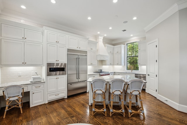 3202 Mid Ln, Houston, TX 77027 - kitchen with built in appliances, custom range hood, ornamental molding, white cabinets, and a kitchen breakfast bar