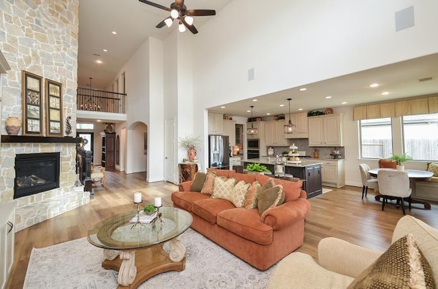 2038 Green Haven Ct, Missouri City, TX 77459 - living area featuring arched walkways, a fireplace, light wood finished floors, a towering ceiling, and a ceiling fan