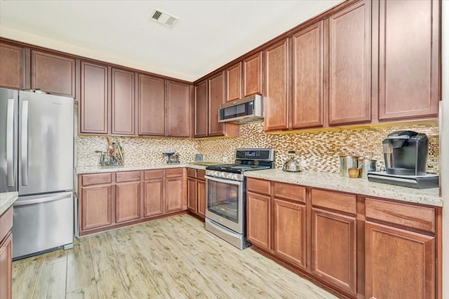 8323 Egret Bay Cir, Baytown, TX 77523 - kitchen with stainless steel appliances, light wood-type flooring, tasteful backsplash, light stone countertops, and brown cabinetry