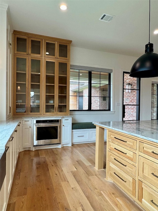 1701 Bayram Dr, Houston, TX 77055 - kitchen featuring stainless steel oven, light stone countertops, glass insert cabinets, light wood-style flooring, and recessed lighting