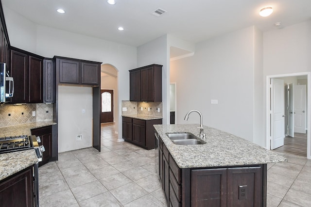 11819 Eagle Ridge Dr, Mont Belvieu, TX 77535 - kitchen featuring a sink, arched walkways, decorative backsplash, light tile patterned floors, and light stone counters