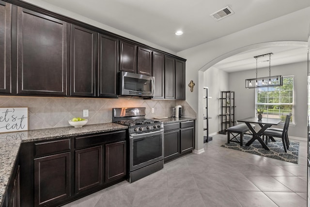 2525 Galley Ridge Dr, La Marque, TX 77568 - kitchen featuring appliances with stainless steel finishes, arched walkways, tasteful backsplash, light stone countertops, and dark brown cabinetry