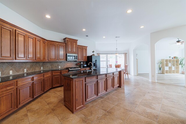 26122 Savory Springs Ln, Katy, TX 77494 - kitchen featuring stainless steel appliances, arched walkways, brown cabinets, backsplash, and a kitchen island with sink
