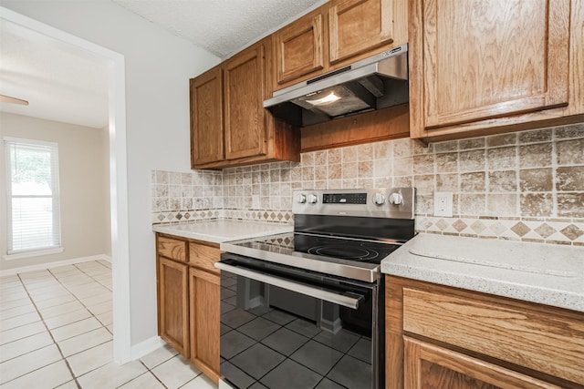 22519 Elkana Deane Ln, Katy, TX 77449 - kitchen with electric range, under cabinet range hood, light tile patterned floors, brown cabinets, and decorative backsplash
