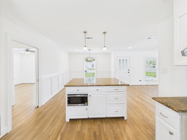 4927 Ward St, Houston, TX 77021 - kitchen with stainless steel microwave, light wood-type flooring, white cabinetry, ornamental molding, and plenty of natural light
