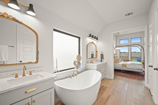 19002 Valentine Padlock Cir, Tomball, TX 77377 - ensuite bathroom featuring wood finished floors, two vanities, a freestanding bath, vaulted ceiling, and baseboards