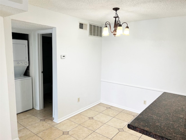 12550 Whittington Dr Unit 712, Houston, TX 77077 - unfurnished dining area featuring stacked washer / drying machine, light tile patterned flooring, a chandelier, a textured ceiling, and baseboards