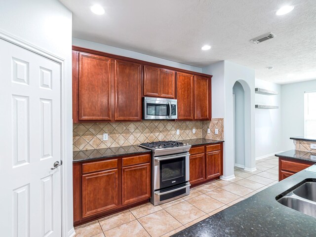 25203 Auburn Terrace Dr, Spring, TX 77389 - kitchen with appliances with stainless steel finishes, backsplash, light tile patterned flooring, arched walkways, and dark stone countertops
