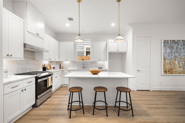 5238 Larkin St, Houston, TX 77007 - kitchen featuring stainless steel gas range, under cabinet range hood, backsplash, white cabinets, and a kitchen breakfast bar