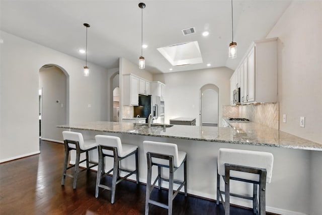 22907 Caverly Ln, Tomball, TX 77375 - kitchen featuring arched walkways, a peninsula, stainless steel microwave, tasteful backsplash, and light stone countertops