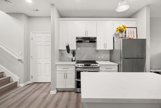 8534 Woodlyn Rd, Houston, TX 77028 - kitchen with appliances with stainless steel finishes, under cabinet range hood, light wood-type flooring, white cabinetry, and tasteful backsplash