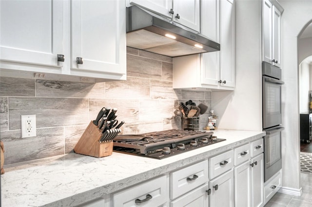 8507 Marchelle Ln, Spring, TX 77379 - kitchen with under cabinet range hood, stainless steel appliances, arched walkways, and decorative backsplash