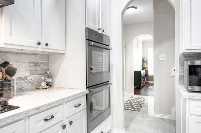8507 Marchelle Ln, Spring, TX 77379 - kitchen featuring arched walkways, stainless steel appliances, backsplash, white cabinetry, and baseboards