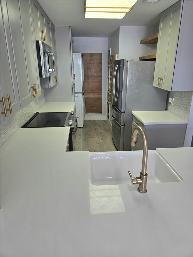 7700 Seawall Blvd Unit 409, Galveston, TX 77551 - kitchen with appliances with stainless steel finishes, a sink, open shelves, light countertops, and light wood-style floors