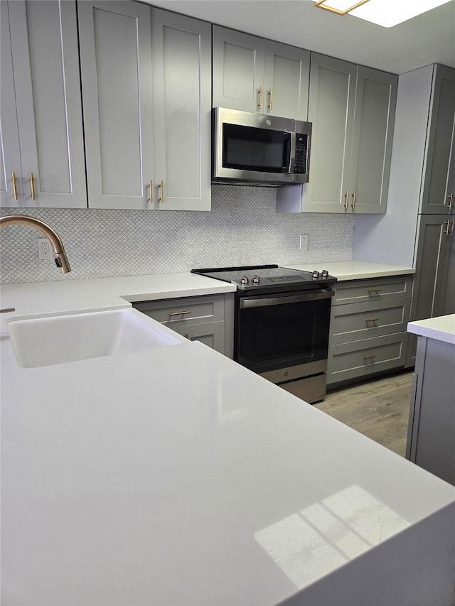 7700 Seawall Blvd Unit 409, Galveston, TX 77551 - kitchen featuring appliances with stainless steel finishes, gray cabinets, decorative backsplash, and light countertops