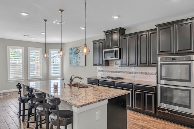 5803 Platinum Lakes Ct, Rosenberg, TX 77469 - kitchen with appliances with stainless steel finishes, a sink, light stone countertops, a kitchen island with sink, and light wood-type flooring