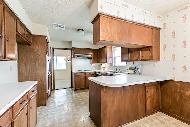 15419 Diana Ln, Houston, TX 77062 - kitchen with a peninsula, a textured ceiling, wallpapered walls, under cabinet range hood, and plenty of natural light
