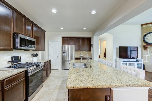223 Summer Gate Ct, Rosenberg, TX 77469 - kitchen featuring stainless steel appliances, a sink, backsplash, light stone countertops, and a center island with sink