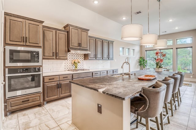 1010 Zoyas Creek Trl, Katy, TX 77494 - kitchen featuring appliances with stainless steel finishes, a sink, backsplash, a kitchen island with sink, and a kitchen breakfast bar