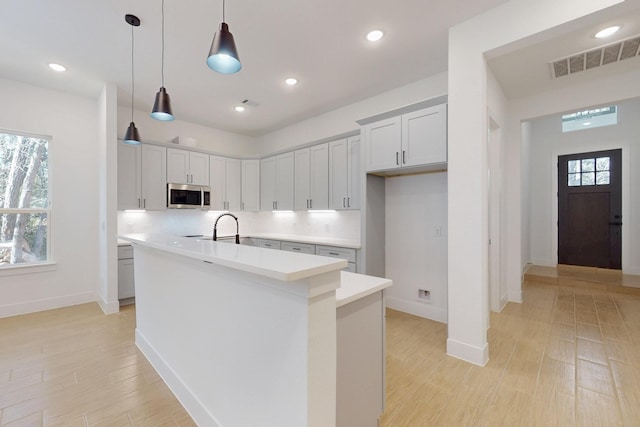 117 Keaau Ct, Bastrop, TX 78602 - kitchen with stainless steel microwave, an island with sink, light countertops, plenty of natural light, and recessed lighting