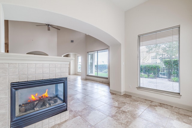 403 Harborside Way, Kemah, TX 77565 - unfurnished living room with ceiling fan, arched walkways, baseboards, a towering ceiling, and a tiled fireplace