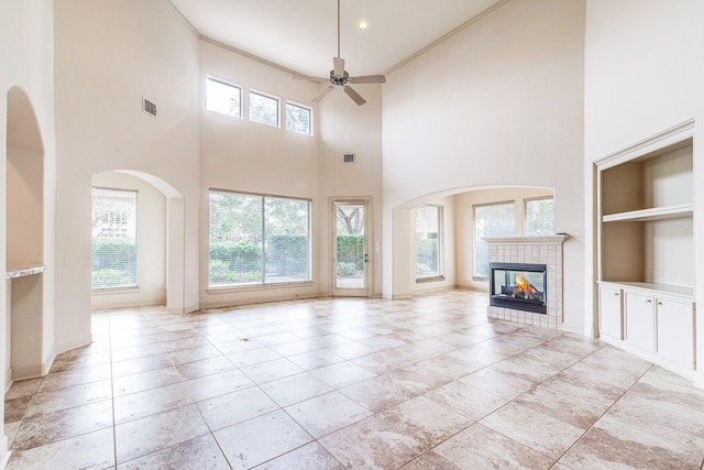 403 Harborside Way, Kemah, TX 77565 - unfurnished living room with built in shelves, ceiling fan, a tiled fireplace, a towering ceiling, and baseboards