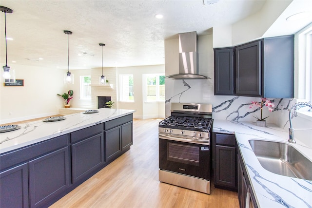 12419 Huntington Field Dr, Houston, TX 77099 - kitchen featuring stainless steel gas range, wall chimney exhaust hood, light wood-style flooring, a sink, and a textured ceiling