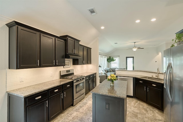 2947 Twin Cove Ct, Conroe, TX 77301 - kitchen with appliances with stainless steel finishes, lofted ceiling, backsplash, light stone counters, and a center island