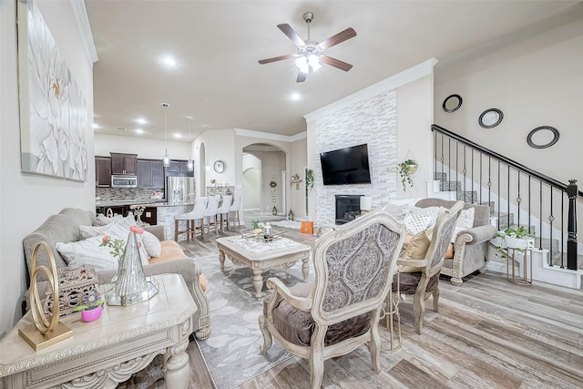9103 Acorn Harvest Trl, Richmond, TX 77407 - living room with ornamental molding, arched walkways, ceiling fan, stairs, and a stone fireplace