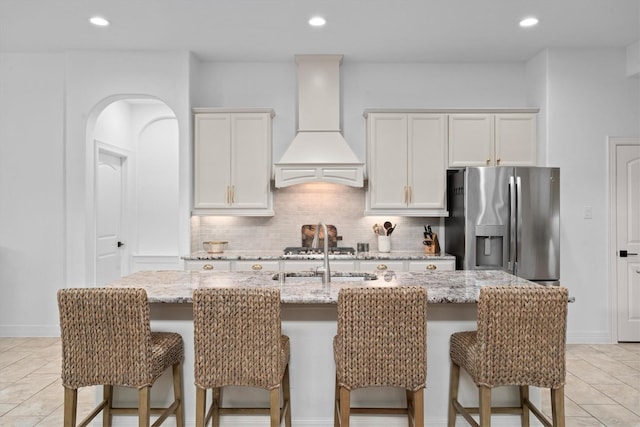 27121 Holtwood Grove Rd, Magnolia, TX 77354 - kitchen featuring premium range hood, an island with sink, light tile patterned flooring, a breakfast bar, and stainless steel fridge with ice dispenser