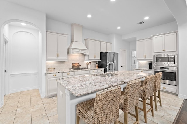 27121 Holtwood Grove Rd, Magnolia, TX 77354 - kitchen featuring stainless steel appliances, a sink, custom exhaust hood, backsplash, and a kitchen breakfast bar