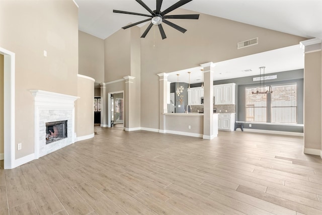 3106 Five Oaks Dr, Missouri City, TX 77459 - unfurnished living room with ceiling fan, a chandelier, a stone fireplace, light wood-style floors, and high vaulted ceiling