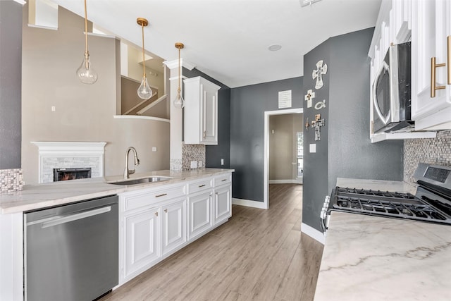 3106 Five Oaks Dr, Missouri City, TX 77459 - kitchen with stainless steel appliances, tasteful backsplash, a stone fireplace, white cabinetry, and light wood-style floors