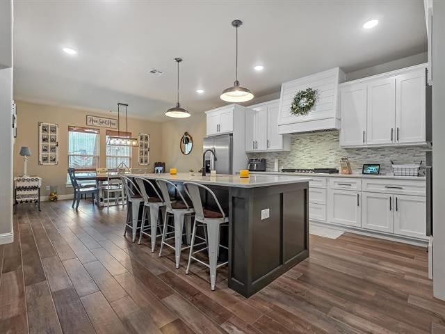 14845 Norma Jane Ln, Beaumont, TX 77713 - kitchen with stainless steel fridge, dark wood-style floors, custom exhaust hood, backsplash, and white cabinetry