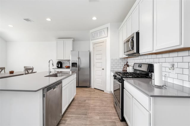 8219 Molasses Way, Rosharon, TX 77583 - kitchen with appliances with stainless steel finishes, a sink, light wood-style flooring, decorative backsplash, and a kitchen island with sink