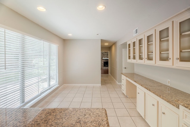 5206 Graystone Ln, Houston, TX 77069 - kitchen with light tile patterned flooring, glass insert cabinets, light stone countertops, baseboards, and a fireplace with raised hearth