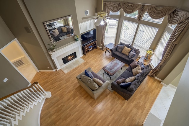 11802 Rue Saint Honore Ct, Tomball, TX 77377 - living room featuring a premium fireplace, ceiling fan, light wood-style flooring, baseboards, and a towering ceiling