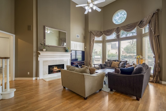 11802 Rue Saint Honore Ct, Tomball, TX 77377 - living room featuring a ceiling fan, a towering ceiling, a premium fireplace, baseboards, and light wood-style floors