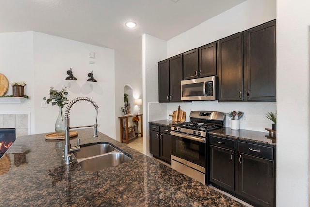 9998 Chimney Swift Ln, Conroe, TX 77385 - kitchen featuring stainless steel appliances, a sink, dark stone counters, arched walkways, and a tile fireplace