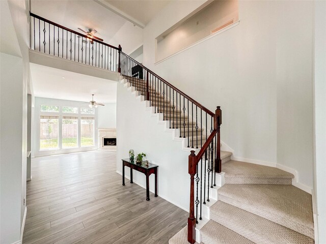 6081 Trent Ct, League City, TX 77573 - staircase featuring a ceiling fan, a fireplace, a high ceiling, wood finished floors, and baseboards