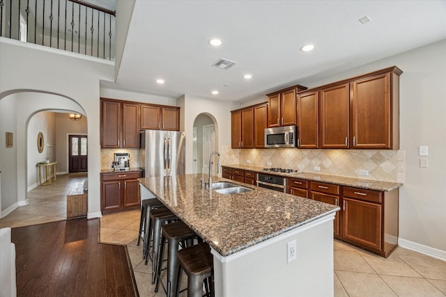 9982 Manor Spring Ln, Brookshire, TX 77423 - kitchen featuring appliances with stainless steel finishes, arched walkways, a sink, dark stone countertops, and a kitchen breakfast bar
